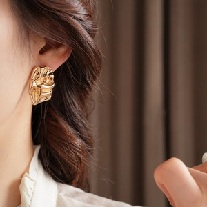 Detailed close-up of golden irregular pleated metal earring worn on ear with soft lighting