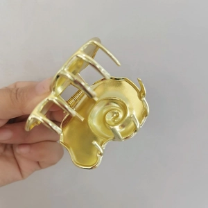 Macro detail of a golden shell-shaped hair claw clip with a strong metal spring