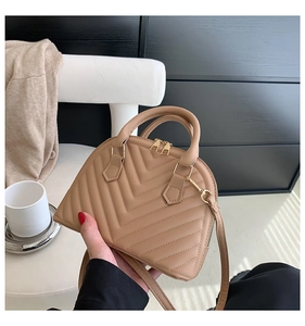 Detailed close-up of quilted beige shell bag featuring gold zippers and a slim strap