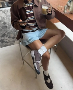 Detalle de minifalda plisada azul claro con chaqueta marrón para un look urbano chic