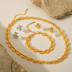 Golden seashell jewelry set with necklace, bracelet and pearl earrings on stone