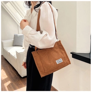 Brown corduroy shoulder tote bag with adjustable strap and front pocket detail on model