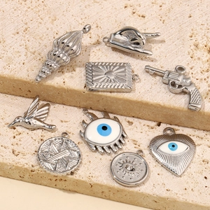 Assorted stainless steel charms including hummingbird and evil eye on stone surface