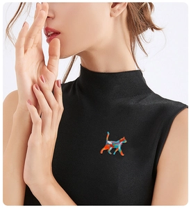 Close-up of a colorful enamel cat brooch pinned on a black sleeveless top with white background