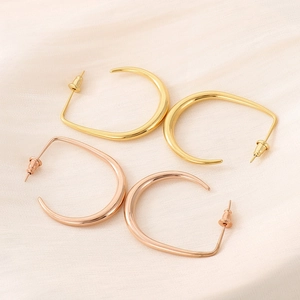 Detailed view of U-shaped gold and rose gold titanium steel earrings on pink silk fabric