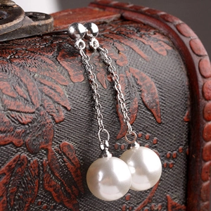 Elegant long tassel pearl earrings with silver chains on a vintage wooden jewelry box