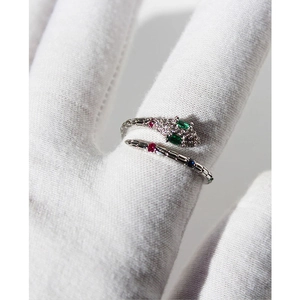 Silver snake ring with green stone eyes and colorful crystals on a hand with white glove