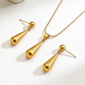 Poliertes goldenes Schmuckset mit Wassertropfen-Anhänger und passenden Ohrringen auf weiß