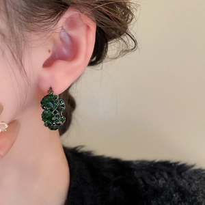 Close-up of vintage emerald green crystal hoop earrings on a model with a soft focus background