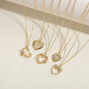 Golden heart pendant necklaces with pearls and zircons displayed on a beige background