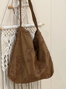 Detail of floral embroidery on a brown suede shoulder bag hanging on a macrame wall