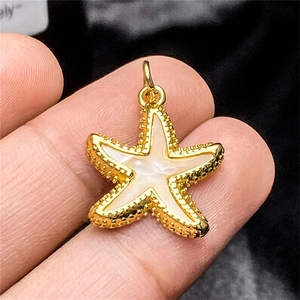 Macro shot of gold starfish pendant with white enamel inlay held between fingers