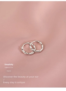 Close-up of minimalist silver bamboo knot earrings on soft pink satin fabric