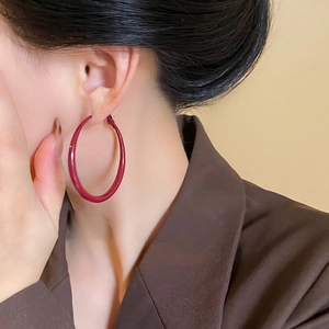 Close-up of model wearing large Ankara red geometric hoop earrings with a glossy finish