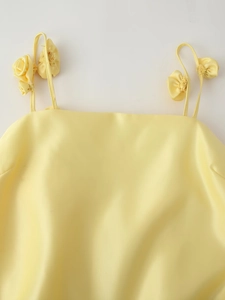 Close-up of yellow satin dress featuring delicate floral shoulder strap detailing