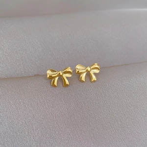 Detailed view of golden bow stud earrings made of titanium steel on silk fabric
