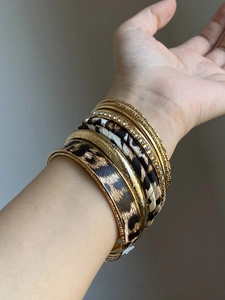 Close-up of women wearing stacked leopard print leather and gold metallic bangle set