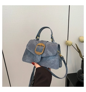 Detail of blue denim crossbody bag featuring a large textured gold buckle on the front flap