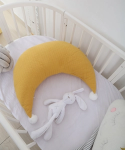 Close-up of ginger moon-shaped baby pillow with white pom-poms on quilted cotton fabric