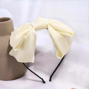 Close-up of a premium beige satin oversized bow hair clip with glossy fabric texture
