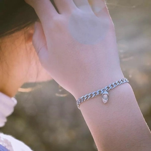 Close-up of a silver chain bracelet with oval pendant worn on a wrist in natural light