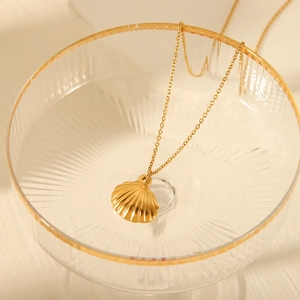 Golden scallop shell pendant necklace displayed in a decorative glass bowl detail