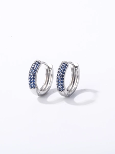 Détail de boucles d'oreilles créoles argentées serties de cristaux bleus