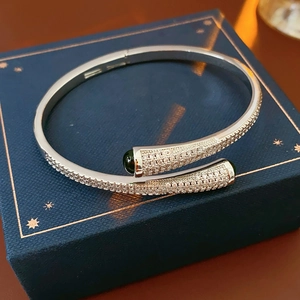 Macro detail of silver-toned open bangle with green gems on a navy velvet gift box