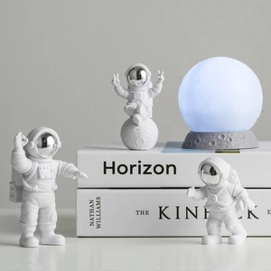 Three white resin astronaut figurines and a glowing moon lamp on stacked books