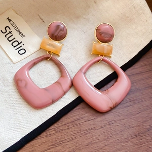 Detail of resin geometric earrings with pink and orange marble texture and gold metal studs