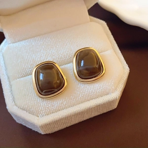 Macro view of gold-plated tiger eye earrings in a white velvet hexagonal jewelry box