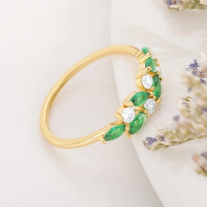 Macro detail of gold ring with marquise green emeralds and round white gemstones