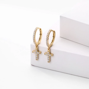 Macro detail of gold cross earrings with sparkling zircon stones on a white background