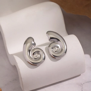 Macro shot of silver swirl spiral earrings on a wavy white ceramic display stand