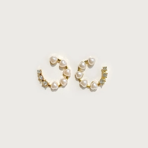 Detail of C-shaped gold earrings featuring white heart pearls and sparkling zircons