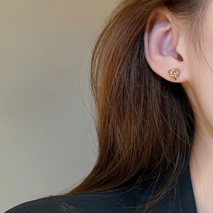 Close-up of golden heart knot earrings worn on a model's ear showing detailed metal texture