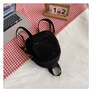 Detail of black corduroy mini backpack on a plaid mat with laptop and wooden calendar
