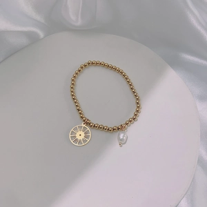 Detail view of gold beaded bracelet with sun charm and teardrop pearl on white silk background