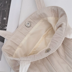 Detalle del bolso tipo cubo plisado beige con cierre seguro de doble botón magnético
