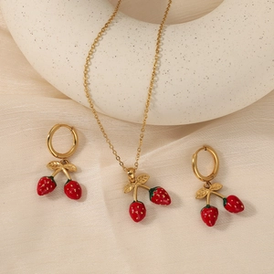 Parure fraise dorée avec collier en émail rouge et boucles d'oreilles sur tissu beige