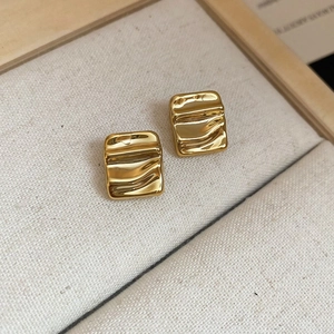 Macro shot of gold square earrings with wavy texture inside a beige linen jewelry box