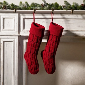 Pair of red knitted Christmas stockings hanging on fireplace with festive pine cones