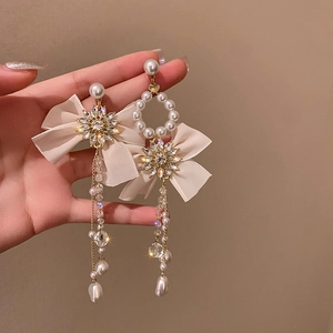 Close-up of beige ribbon bow earrings with cascading crystal fringe and pearls