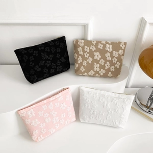 Floral embossed cosmetic bags in black, beige, pink, and white on a white tiered display