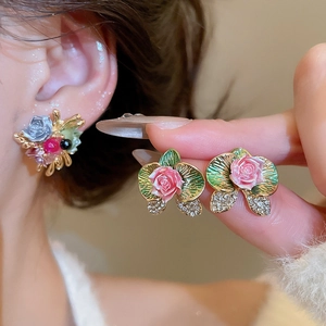 Macro shot of floral earrings with pink rose, green orchid motifs and white diamonds