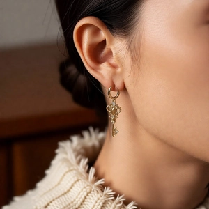 Detail of vintage gold key earrings with zircons worn by a model in a cozy sweater