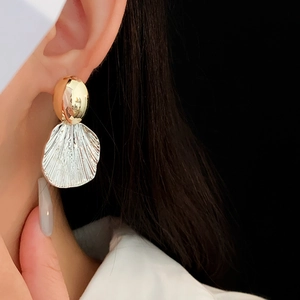 Close-up of model wearing gold and silver pleated shell earrings on black background