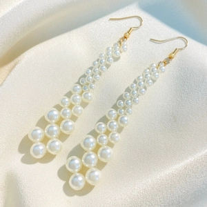 Macro shot of long pearl drop earrings with gold hooks on elegant silk fabric