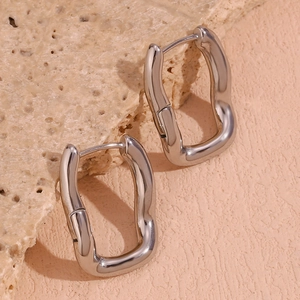 Close-up of silver irregular wave hoop earrings displayed on a natural stone background