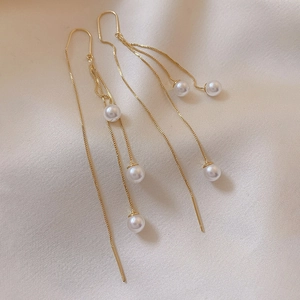 Detailed view of long gold tassel earrings with elegant white pearls on soft fabric